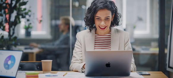 A professional woman working in a modern office, smiling at her Apple computer.